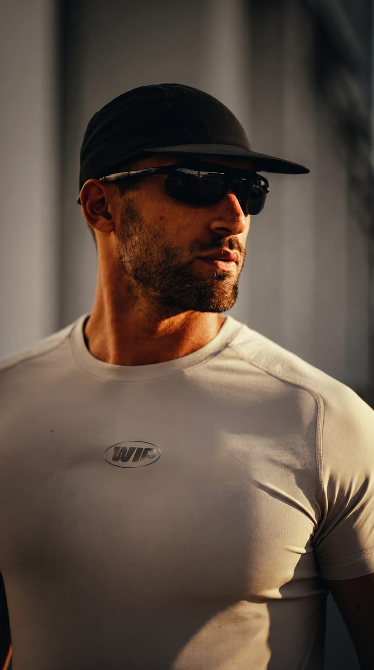 Homem de boné e óculos esportivos vestindo camiseta de treino clara com o logotipo WIP no peito